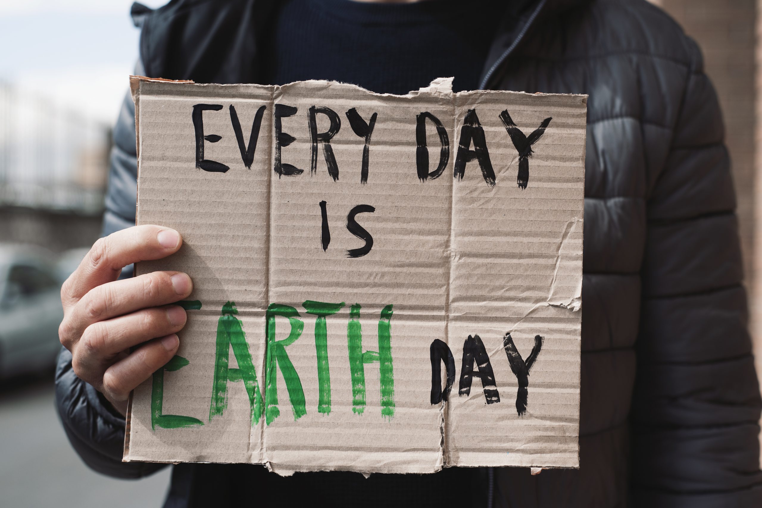 一个年轻的白人男子在街上展示一个棕色纸板招牌，上面写着“每天都是地球日”